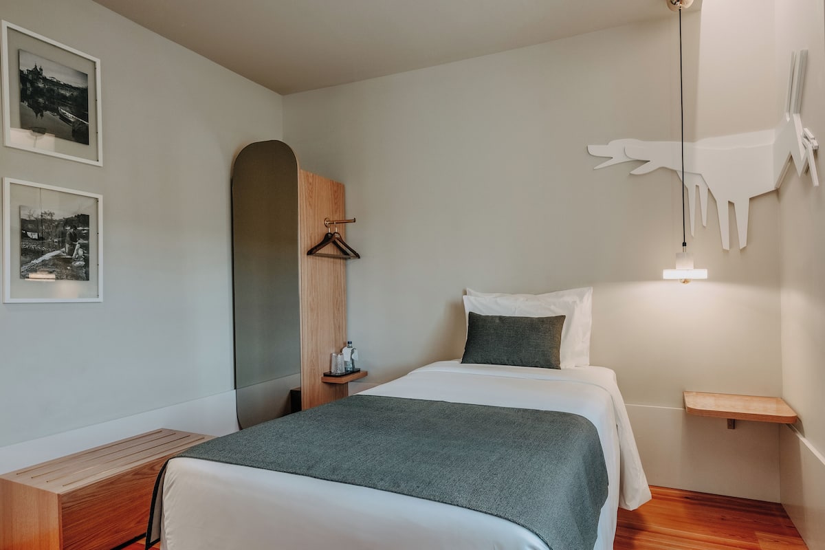 Un dormitorio moderno con una cama, un banco de madera, un perchero y dos cuadros en la pared.