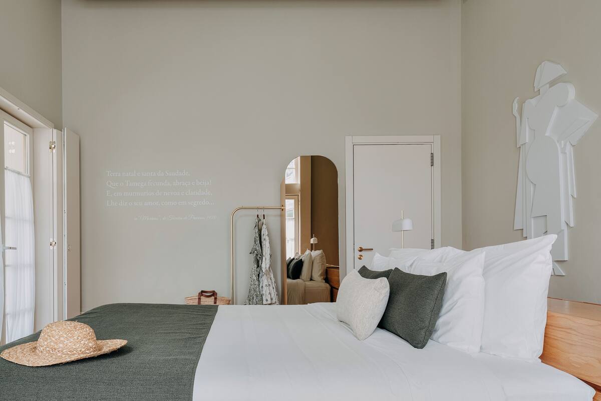 Un dormitorio con una cama, almohadas, un sombrero, un espejo y una pared con texto.