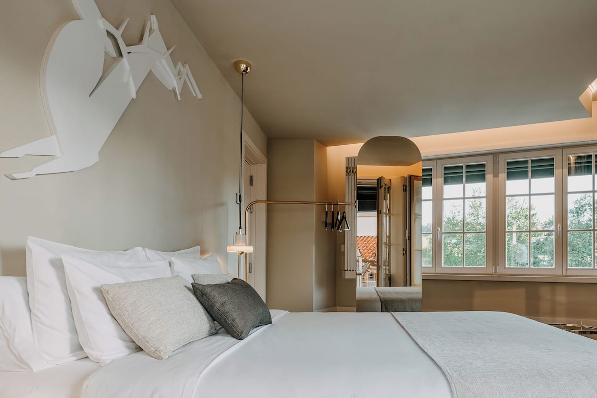 Habitación de hotel moderna con una cama grande, una obra de arte original en la pared, una lámpara de techo y vistas a través de un arco.