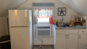 Una cocina compacta con refrigerador, una ventana con cortina, aire acondicionado de pared y una decoración con forma de estrella de mar.