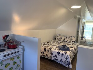 Quarto compacto com cozinha compacta, uma cama com colcha temática e vista para o exterior.