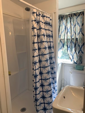Casa de banho com cortina de chuveiro, pia e janela com cortinas estampadas.