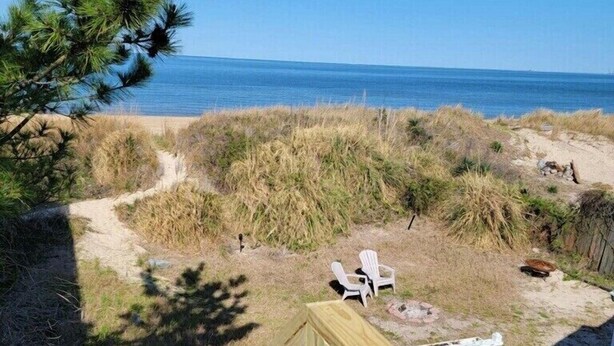 Una terraza de madera con barandilla que da a una playa con dunas y una vista despejada del océano.