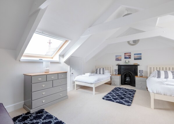 A bedroom with a sloped ceiling, a skylight, a fireplace, a bed, a dresser, and a nightstand.
