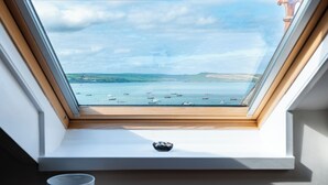 A skylight with a view of a coastal area, including boats on the water and distant hills. - The Terrace 2 (Wadebridge)