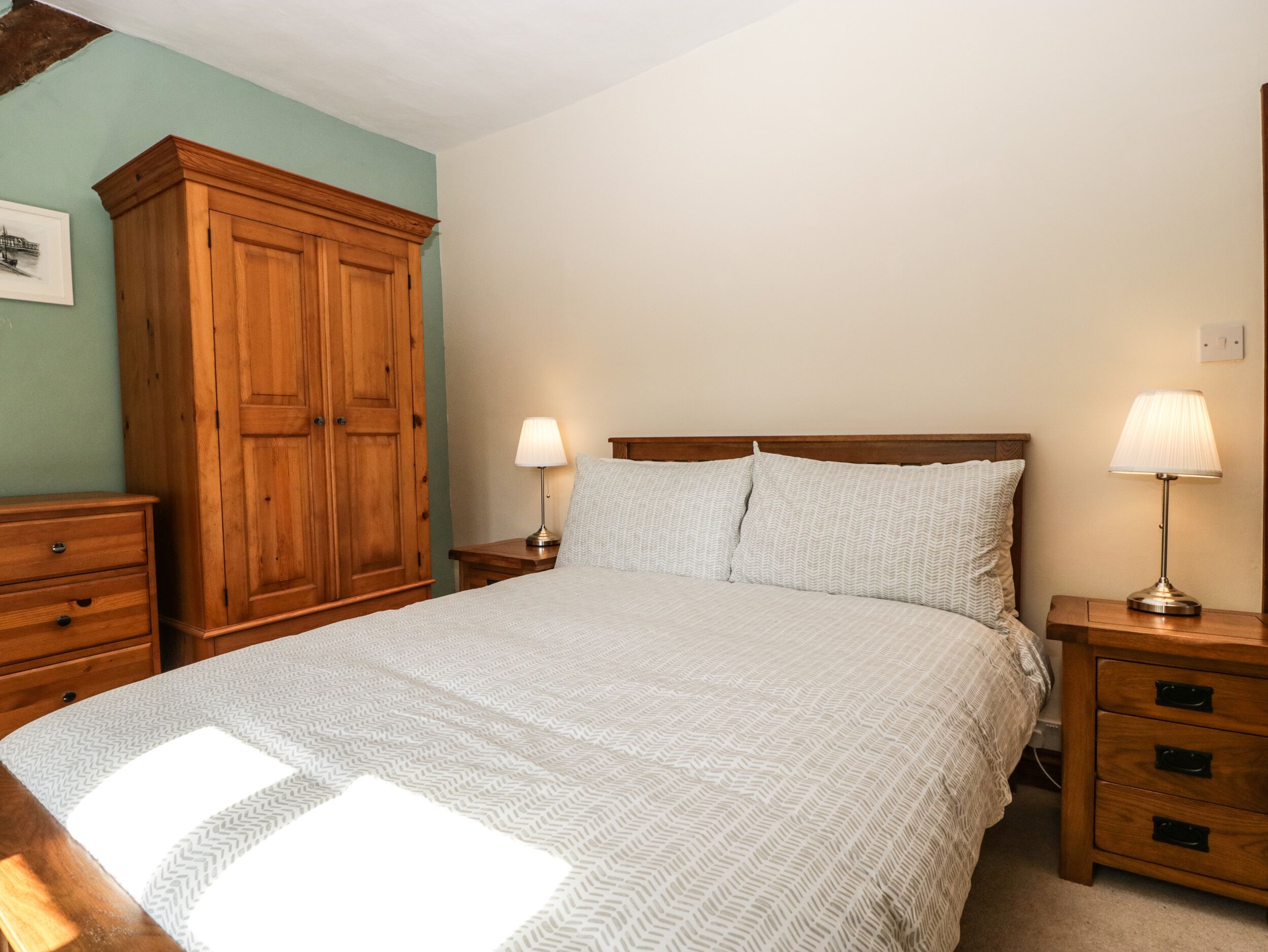 A bedroom with a large bed, wooden wardrobe, two bedside tables with lamps, and a small bedside table with a lamp.