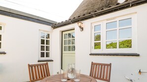A round wooden table with two chairs, a glass pitcher, and a candle holder on a patio with a white wall and windows. - 1 Old Thatch (Bridgwater)