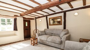 A cozy room with a wooden ceiling, a sofa, a chair, and a small table. - 1 Old Thatch (Bridgwater)