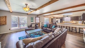 A spacious living area with a large leather sofa, a coffee table, and a ceiling fan. There is a kitchen area with a bar and stools.