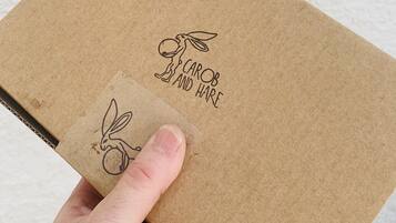 Une main tenant une boîte en carton marron ornée d’une illustration de lapin et portant l’inscription « CAROB AND HARE ».