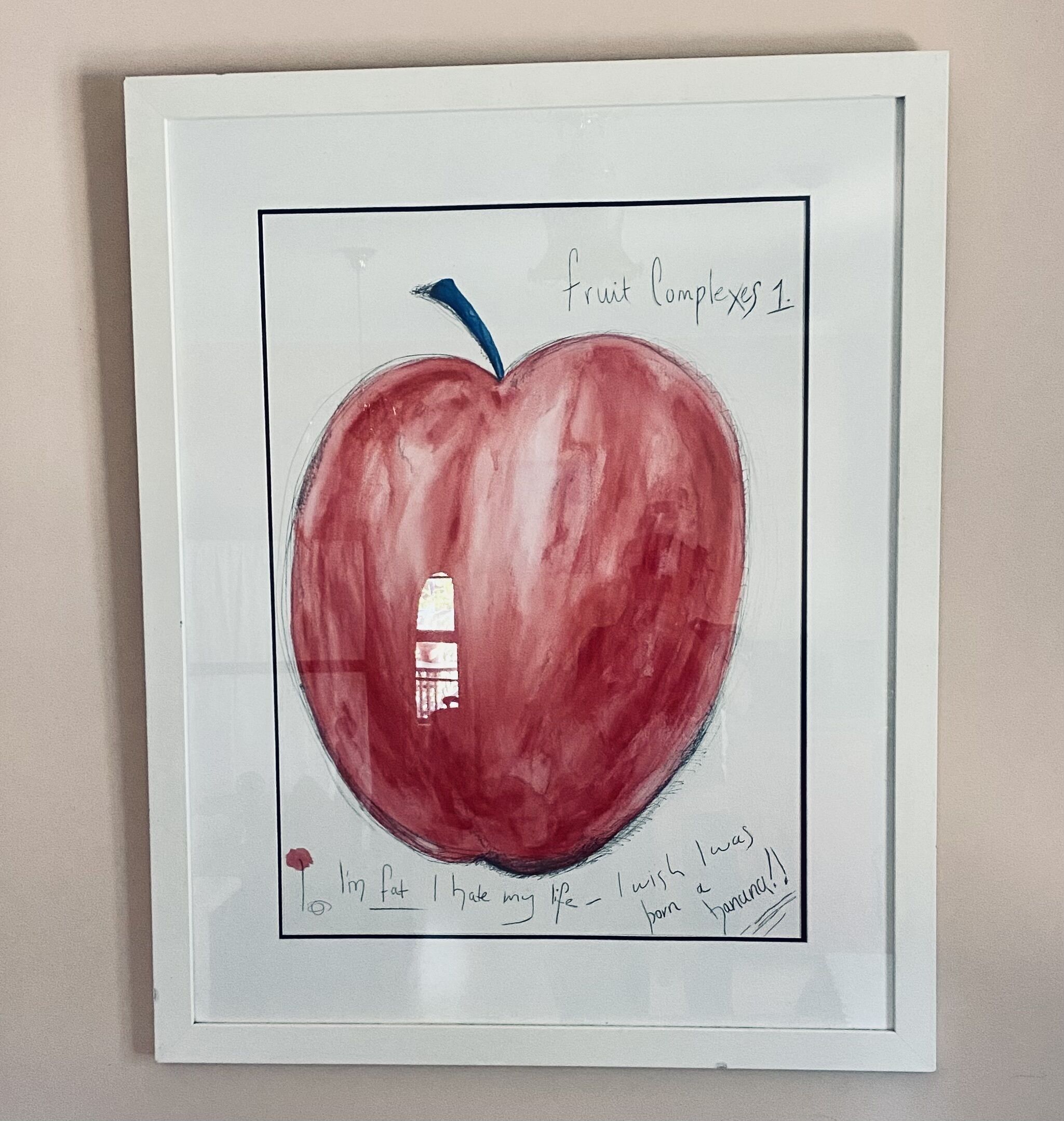 Ein gerahmtes Kunstwerk mit einem roten Apfel, einem blauen Stiel und handschriftlichem Text darunter.