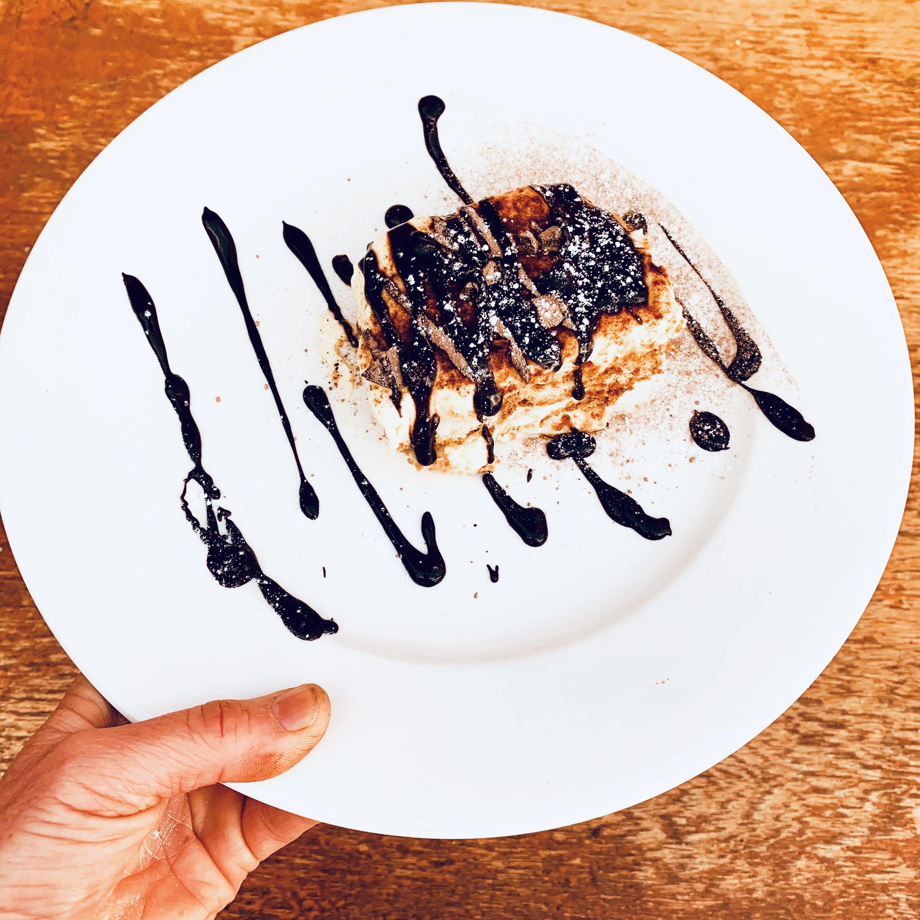 A dessert on a white plate with chocolate drizzle and powdered sugar.