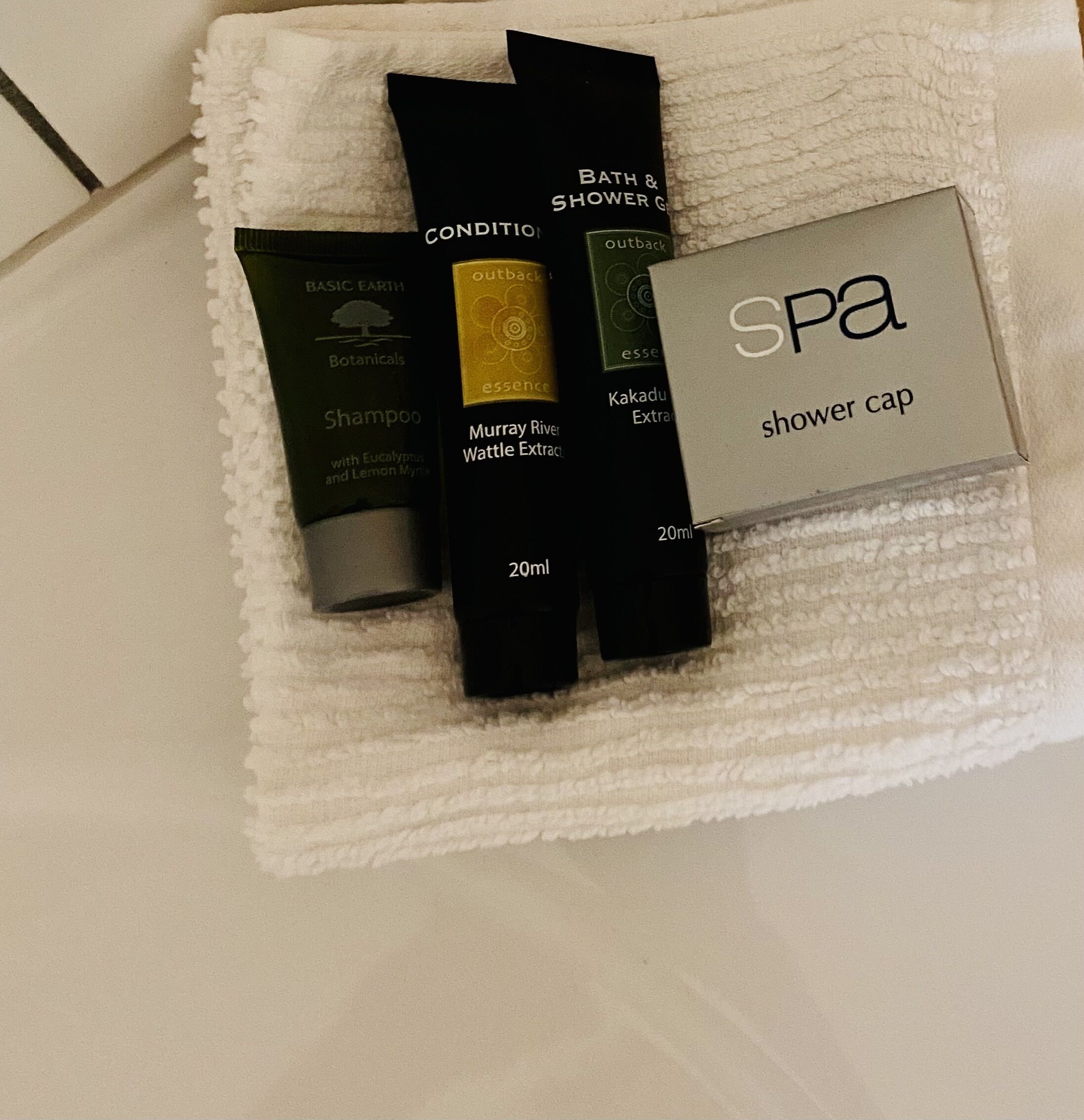 A white towel with various toiletries including a shampoo bottle, a shower cap, and a bottle of essential oil.
