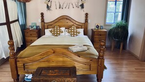 A wooden bed with a carved headboard, a bedside table, a nightstand, a decorative chest, and a hanging plant. - Cute Cosy Cottages – Your Perfect Pet-Friendly Getaway in the Adelaide Hills (Kanmantoo)