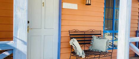 Un porche con una puerta blanca, un banco con cojines y una ventana azul.