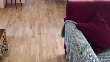Un saló amb terra de fusta, una cadira vermella, un sofà vermell i una manta decorada.
