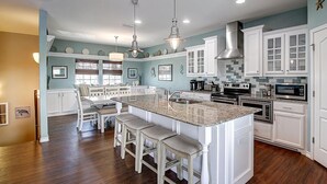 A kitchen with white cabinetry, a granite countertop, and a central island with bar stools. - This spacious home has sophisticated beach decor, adding to the welcoming feel t (Port Aransas)