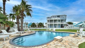 A pool with a stone deck, surrounded by lounge chairs and palm trees. - This spacious home has sophisticated beach decor, adding to the welcoming feel t (Port Aransas)