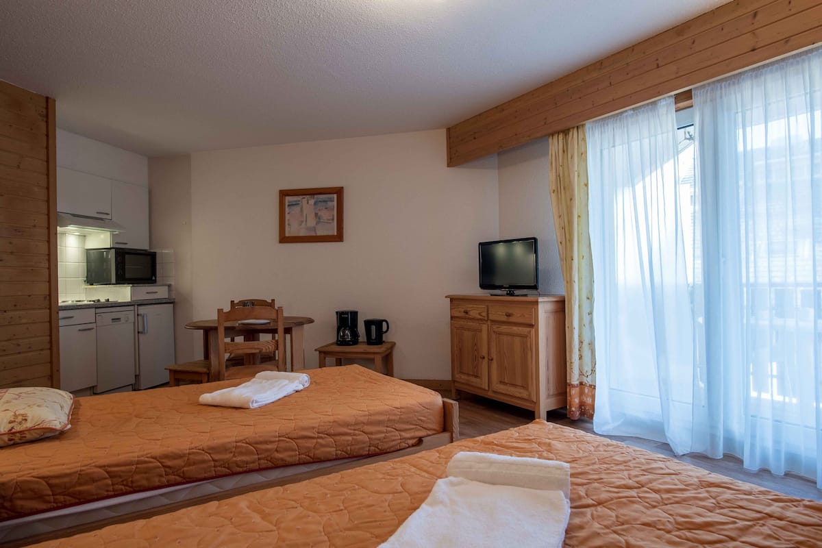 A hotel room with two beds, a TV, a small table with a coffee maker, and a kitchenette.