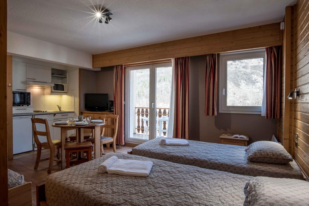 A compact room with two beds, a kitchenette, a dining area, and a television.
