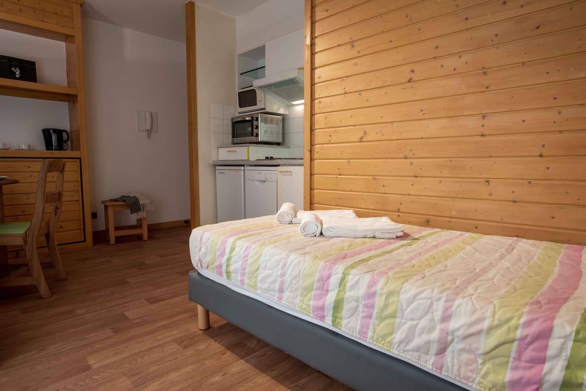 A bedroom with a bed, wooden walls, a small kitchenette, and a wooden chair.