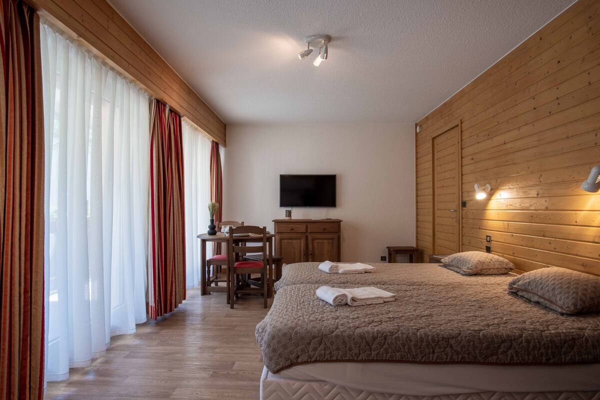 A hotel room with a large bed, a desk with a chair, a television, and wooden paneling on the walls.