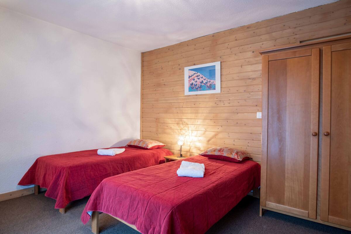 A room with two beds, wooden walls, a wardrobe, and a framed picture on the wall.