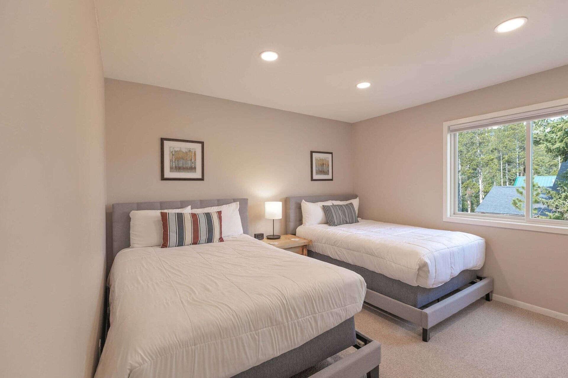 A bedroom with two beds, a window with a view of trees, and two framed pictures on the wall.