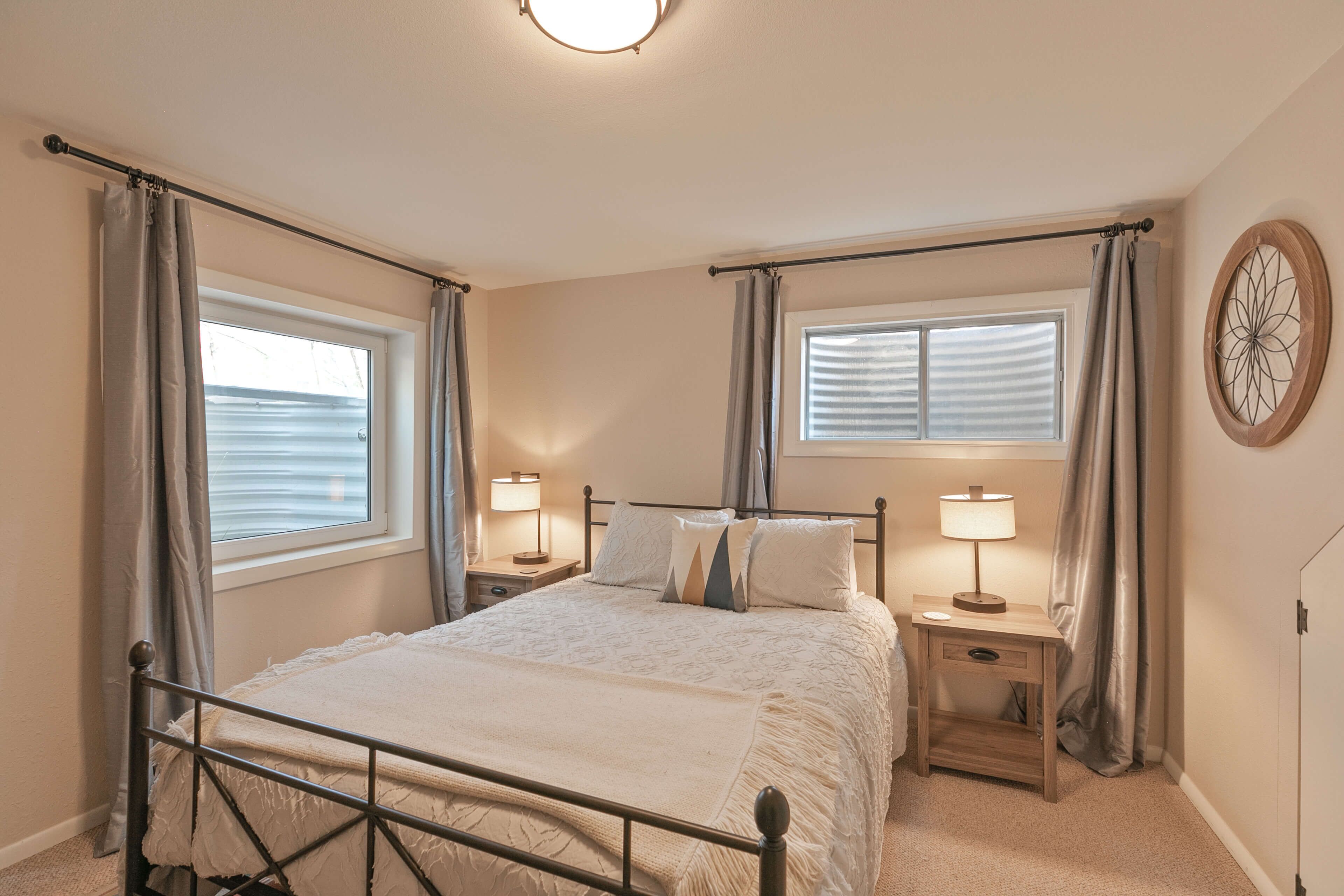 Une chambre à coucher avec un lit, deux tables de chevet avec des lampes, une fenêtre avec des rideaux et une horloge murale.