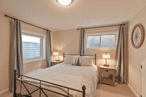 A bedroom with a bed, two bedside tables with lamps, a window with curtains, and a wall clock. - Quicksilver Chalet: Hot Tub, Sleeps 10 (Breckenridge)