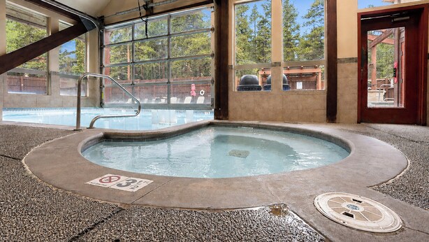 Un espace avec un bain à remous offrant une vue sur la piscine, de grandes fenêtres et une porte en bois.