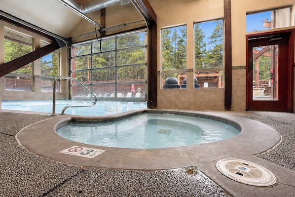 A hot tub area with a view of the pool, large windows, and a wooden door. - Park Place Deer Camp Condo: Ski-In, Walk To Main St, Lift (Breckenridge)