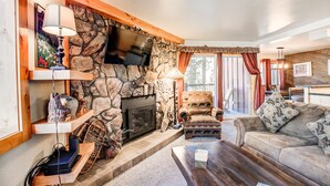 Un salon chaleureux avec une cheminée en pierre, un téléviseur à écran plat fixé au-dessus, et un canapé confortable.