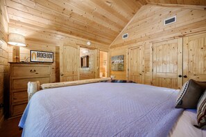 A wooden cabin room with a large bed, a dresser, a sign for Broken Bow Cabin Lodging, and a painting on the wall.