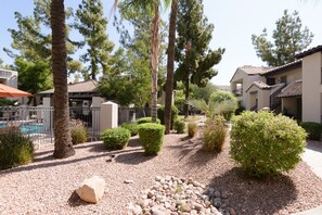 A courtyard with a swimming pool, palm trees, and a building with a tiled roof. - Tastefully Decorated, Perfect Scottsdale Location condo w/ Pool, Spa, Gym! (Scottsdale)