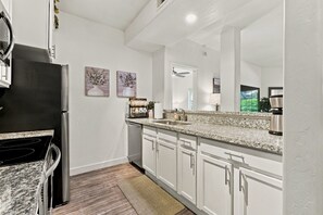 A modern kitchen with white cabinetry, granite countertops, a stainless steel refrigerator, and a built-in oven. - Tastefully Decorated, Perfect Scottsdale Location condo w/ Pool, Spa, Gym! (Scottsdale)