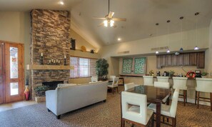 A spacious living area with a stone fireplace, a dining table with chairs, and a kitchen area with cabinets and a countertop.