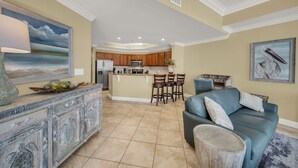 A spacious living area with a blue sofa, a wooden dining table, and a kitchen in the background. - Great Rates*Beach Front Lazy River*Sleeps10*Oasis(formerly PW2) 802*8th floor (Orange Beach)