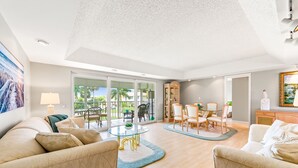 A spacious living room with a glass dining table, beige sofas, and a view of the outdoors. - Glades Golf & Country Club-Large, Updated 2/2 Condo near  Shopping, Beach & Pier (Naples)