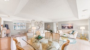 A spacious living area with a glass-top dining table surrounded by chairs, a sofa, and a coffee table with decorative items. - Glades Golf & Country Club-Large, Updated 2/2 Condo near  Shopping, Beach & Pier (Naples)
