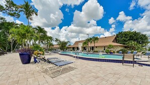 A pool area with lounge chairs, a swimming pool, and palm trees. - Glades Golf & Country Club-Large, Updated 2/2 Condo near  Shopping, Beach & Pier (Naples)