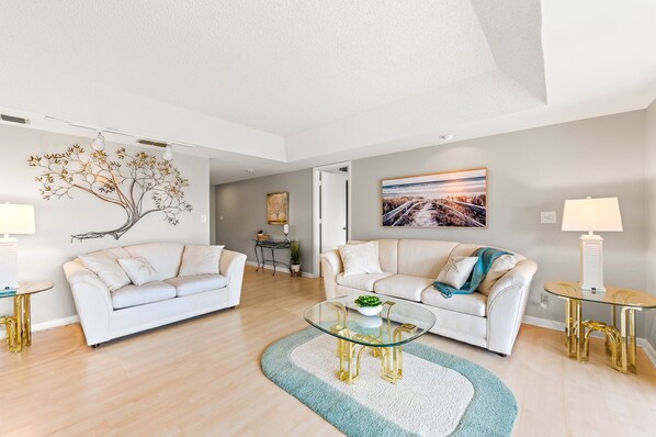A modern living room with two white sofas, a glass coffee table, and a painting on the wall. - Glades Golf & Country Club-Large, Updated 2/2 Condo near Shopping, Beach & Pier (Naples)