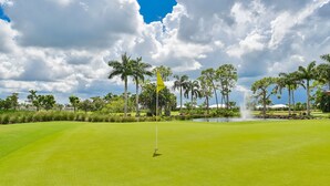 A golf course with a flagstick, palm trees, and a pond. - Glades Golf & Country Club-Large, Updated 2/2 Condo near  Shopping, Beach & Pier (Naples)