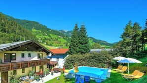 Un chalé con piscina, mobiliario exterior y vistas a las montañas.