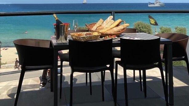 Una mesa con pan y una botella de champán en una terraza con vista al mar.