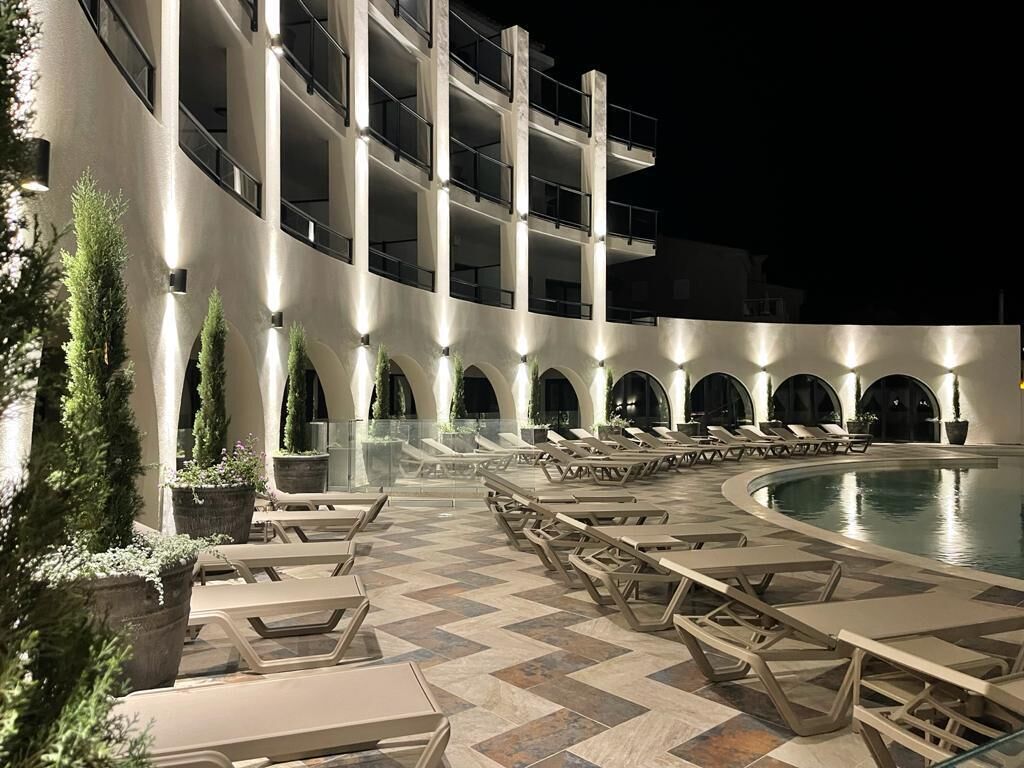 A poolside area with lounge chairs and tables, a pool, and a building with multiple balconies.