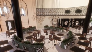 Un espacio interior amplio con diversas disposiciones de asientos, incluyendo mesas redondas y sillas, una pared decorativa central e lámparas esféricas colgantes.