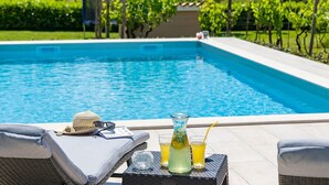 Ein Poolbereich mit Liegestuhl, einem Getränk und einem Glas Saft auf einem Tisch.