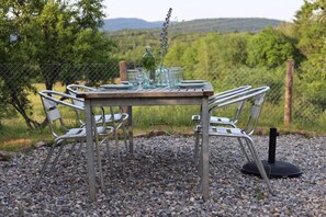 Ein rustikales Essensemble im Freien mit einem Holztisch, Metallstühlen und einem Blumenstrauß.