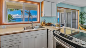A kitchen with a view of the ocean, a stove, and a sink. - Poipu Palms 303 By Parrish Kauai - oceanfront views & walk to beach (Koloa)